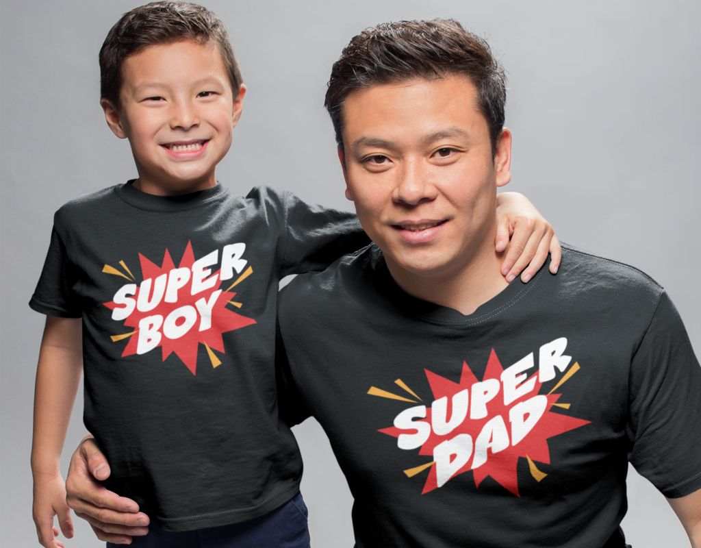 A Father and young son standing in front of a grey background. They are hugging each other and smiling toward the camera
