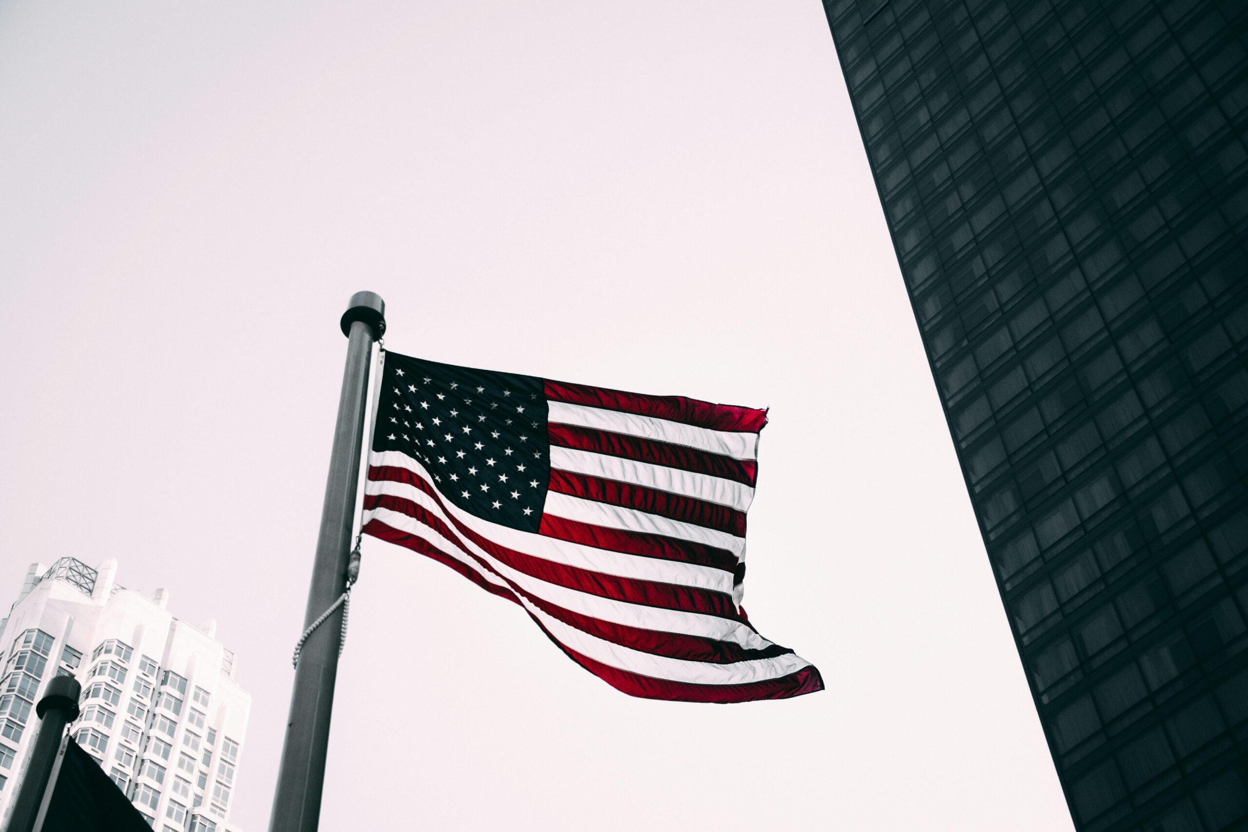 A mostly black and white photo of an American flag on a pole. The Red and blue of the American flag are the only colors other then black and white in the photo